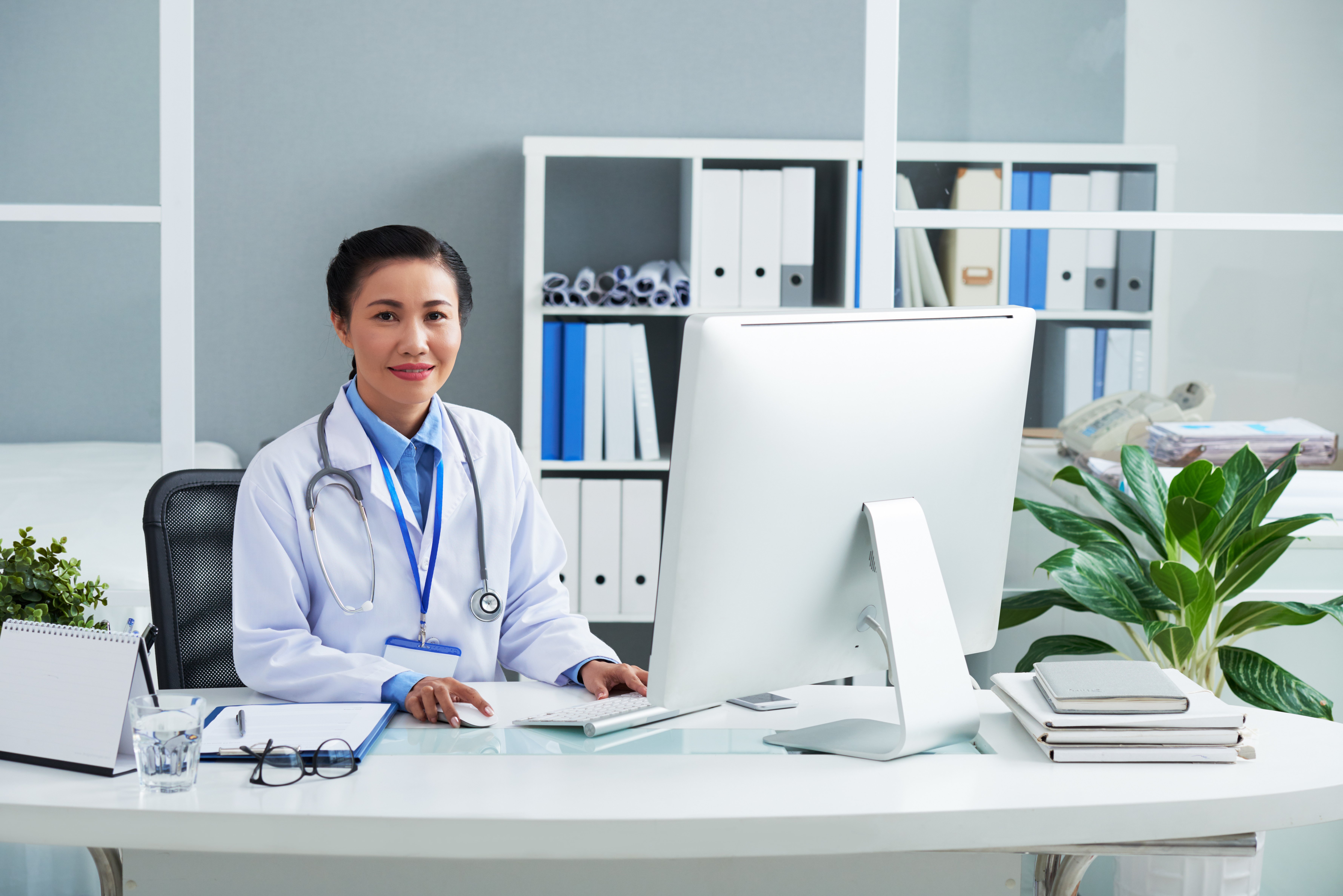 portrait-smiling-general-practitioner-labcoat-working-computer-her-office-desk